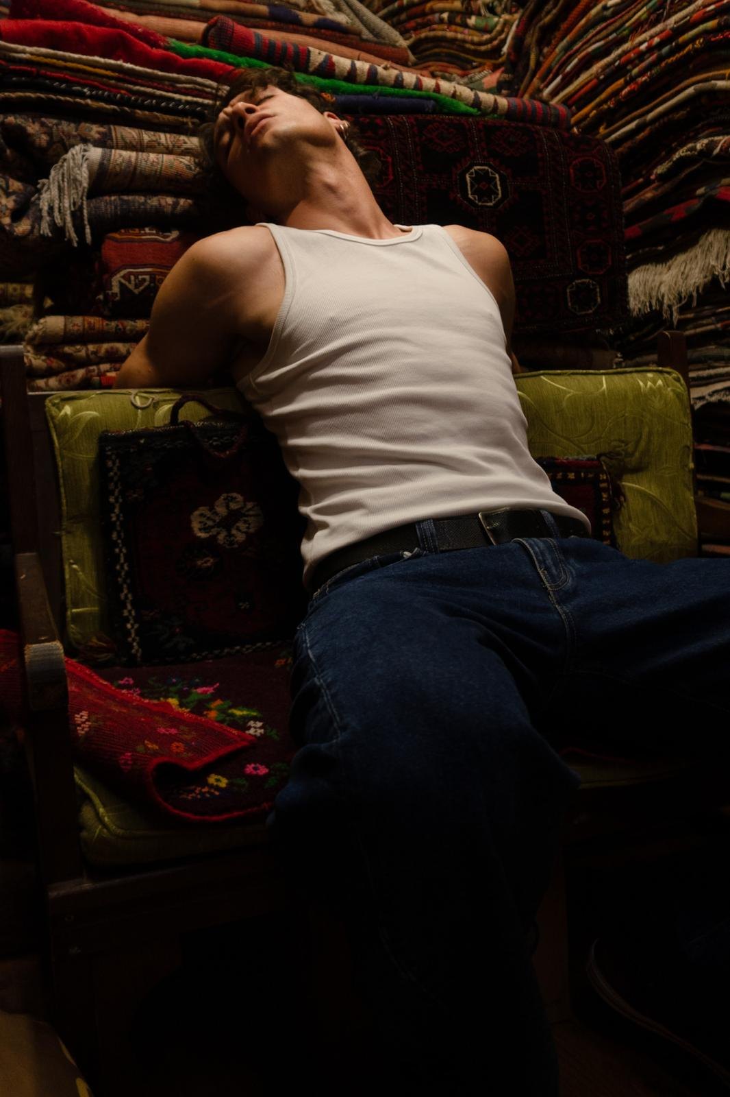 The artisan rests among stacks of Anatolian kilims and rugs